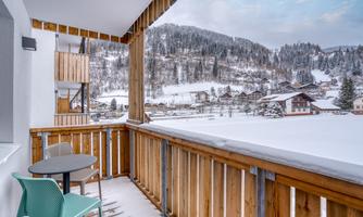 A cozy balcony with a table and chairs, offering a view of snow-covered mountains and cottages. The winter landscape radiates calm and beauty.