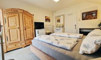 A cozy bedroom with a large bed and a wooden dresser. Pictures hang on the wall, and there is a TV in the room.