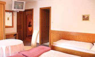 A cozy room with two beds and a table. A television is hanging on the wall, and there is a wooden frame with a picture.