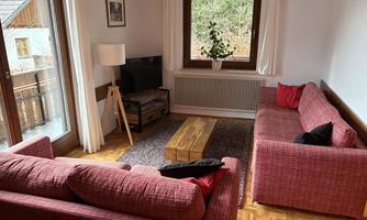 A cozy living space with two red sofas and a wooden table. Large windows offer a view of the greenery and provide plenty of daylight.