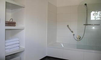 A modern bathroom with a bathtub and shower fixture. Fresh towels are neatly stacked on the shelf.
