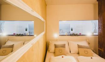 A cozy bedroom with a double bed and soft colors. The room has a large window that lets in light and a decorative mirror wall.