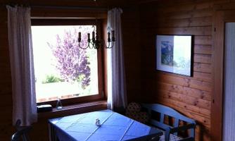 A cozy room with a blue table and chairs. Through the window, you can see a green outdoor area with trees.
