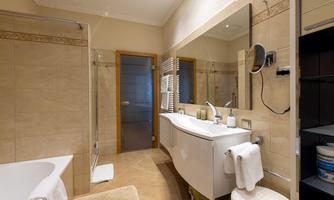 A modern bathroom with a bathtub and a shower. The room is bright with elegant tiles and a large mirror.