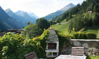 An idyllic mountain landscape with green meadows and impressive peaks. In the foreground is a cozy terrace with a grill.