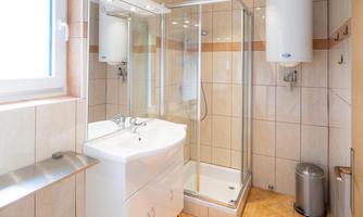 A modern bathroom with a shower cabin, a sink, and a window. The floor is tiled and a yellow bath towel is lying on the floor.