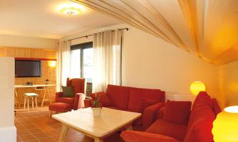 A cozy living room with red sofas and a wooden table. Large windows let in plenty of light and create an inviting atmosphere.