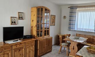 A cozy living space with wooden furniture and a television. Chairs are around a table and a window lets in plenty of daylight.