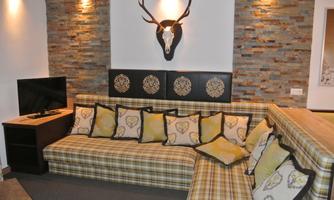 A cozy living room with a large couch and many pillows. A deer antler hangs on the wall above a television.