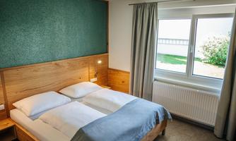 A modern bedroom with a double bed and elegant wood paneling. The window offers a view of the garden and lets in plenty of daylight.