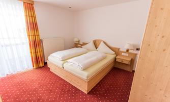 A cozy bedroom with a double bed and two nightstands. The large windows let in a lot of light and give the room a bright atmosphere.