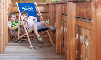 Two children are sitting relaxed on a wooden deck chair. They are enjoying their time on a beautiful wooden terrace.