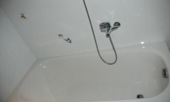 A modern bathtub with a hand shower. The tub is white and placed in a bright bathroom.