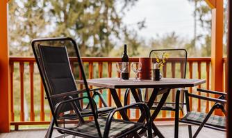 A cozy balcony with a table and chairs. On the table are wine glasses and a bottle of wine next to a blooming plant.