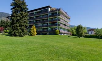 A modern building surrounded by green grass and trees. The sky is clear and blue.