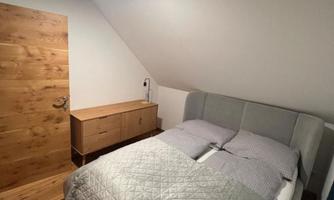 A cozy bedroom with a double bed and a nightstand. The walls are light-colored and the floor is made of wood.