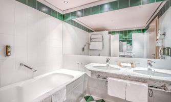 A modern bathroom with a bathtub and a sink made of marble. The walls are tiled in white, with green accents in the tile mirror.