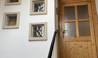 A staircase with a wooden door and the sign "Mittagskogel". Three picture frames hang on the wall, and beneath them is a sun symbol statue.