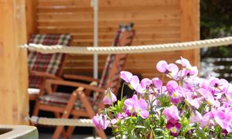 A cozy terrace with blooming pink flowers in the foreground. In the background, two comfortable chairs can be seen.