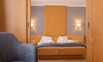 A cozy bedroom with a double bed and modern lighting. In the foreground, there is a gray armchair.
