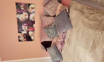 A cozy bedroom with a bed decorated with many pillows. A picture of beautiful roses hangs on the wall.