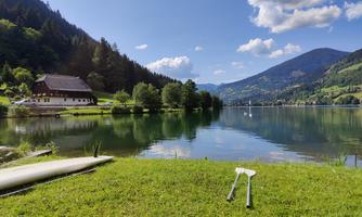 A peaceful lake surrounded by mountains and trees. In the foreground, green grass with a canoe lies.