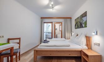 A bright room with two single beds and a wooden chair. Through the window, a door to the balcony is visible.