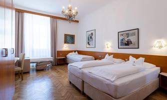 A cozy hotel room with two beds and a modern interior. The room has large windows and a warm wooden design.