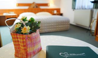 A cozy hotel room with a large bed and a warm atmosphere. On a table, there is a beautiful flower pot and a welcome book.