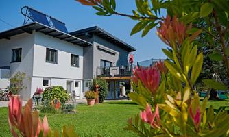 A modern house with solar panels and a well-maintained garden. Colorful plants are blooming in the foreground.