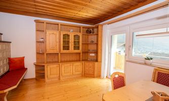 A cozy living space with wooden shelves and a dining table. Large windows provide plenty of daylight.