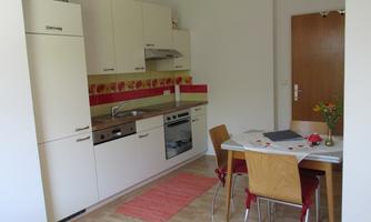 A modern kitchen with bright furniture and a dining area. The room is well-lit and has a friendly design.