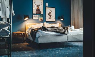 A modern bedroom with a large bed and blue walls.  
Two wall lamps and decorative pictures give the room a cozy atmosphere.