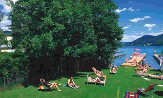 Beautiful meadow by the water with lounge chairs. People relax in the sun under a blue sky.