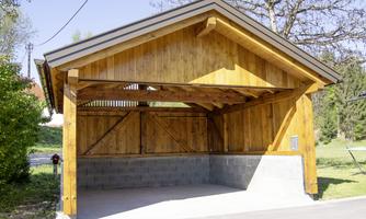 A modern wooden garage with an open front. It stands in a green environment and has a clear, functional style.