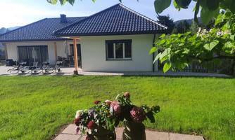 A modern house with a garden and a terrace. In the foreground are two pots with colorful flowers.