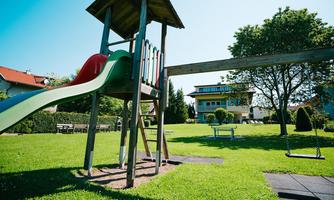 A beautiful playground with a slide and a swing. In the background, there are houses and a lot of green grass.