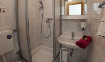 A small bathroom with a shower, sink, and toilet. The walls are brightly tiled, and there is a towel on the sink.