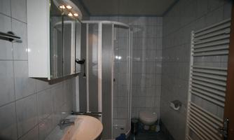 A modern bathroom with a shower, a sink, and a toilet. The walls are decorated with light tiles.