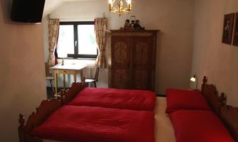 A cozy bedroom with two single beds and red blankets. In the background, there is a table and a wardrobe as well as a window with a view.