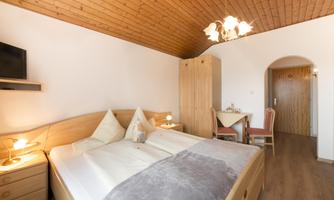 A cozy bedroom with a double bed and wooden ceiling. There is a table with chairs and warm lighting.