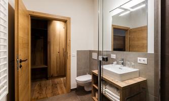 A modern bathroom with wooden details and a large mirror. It features a sink unit and space for towels.