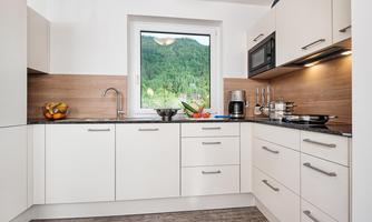 A modern kitchen with white cabinets and a black countertop. A green landscape is visible through the window.