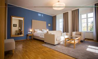 An elegant room with a comfortable sofa, a large bed, and a wooden floor. The walls are painted in a soothing blue and light streams through large windows.