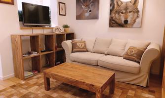A cozy living room with a beige sofa and a wooden table. Pictures of animals hang on the wall and a television is on a wooden shelf.