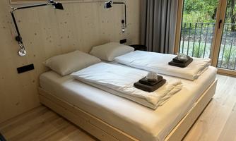 A cozy bedroom with a large double bed and modern nightstands. Large windows offer a view of the greenery.