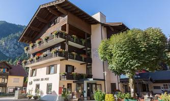 A cozy building with flower boxes and balconies, surrounded by mountains. The facade is inviting and typical of alpine architecture.
