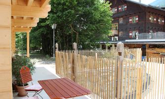 A cozy outdoor area with a small table and chairs. In the background, trees and a traditional building can be seen.