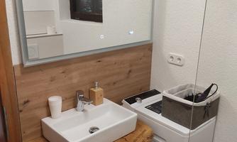 A modern bathroom with a sink on a wooden shelf and a washing machine. There is a large mirror on the wall.