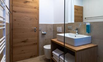 A modern bathroom with a wooden door and an elegant vanity unit. The walls are in neutral tones, and towels are neatly placed.